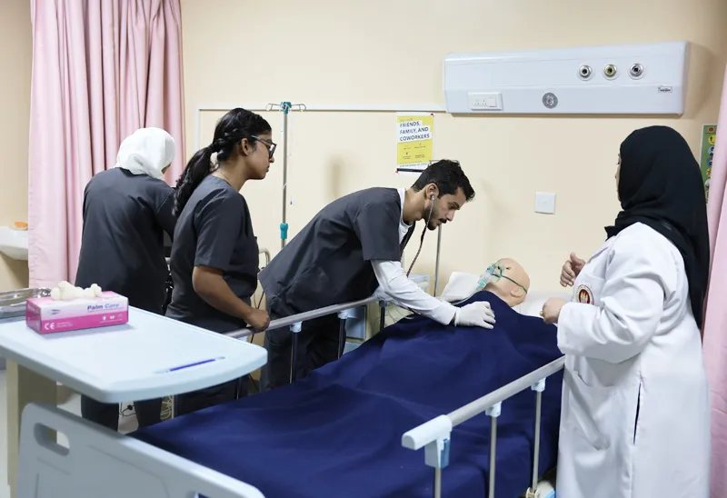 RAKMHSU nursing students at a hospital bed in the skills laboratory, one examining a patient simulator with a stethoscope