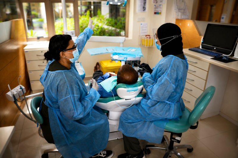 Two RAKMHSU dental students in blue gowns and face masks working either side of a patient reclined in the chair at the college dental clinic