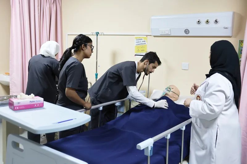 RAKMHSU nursing students at a hospital bed in the skills laboratory, one examining a patient simulator with a stethoscope