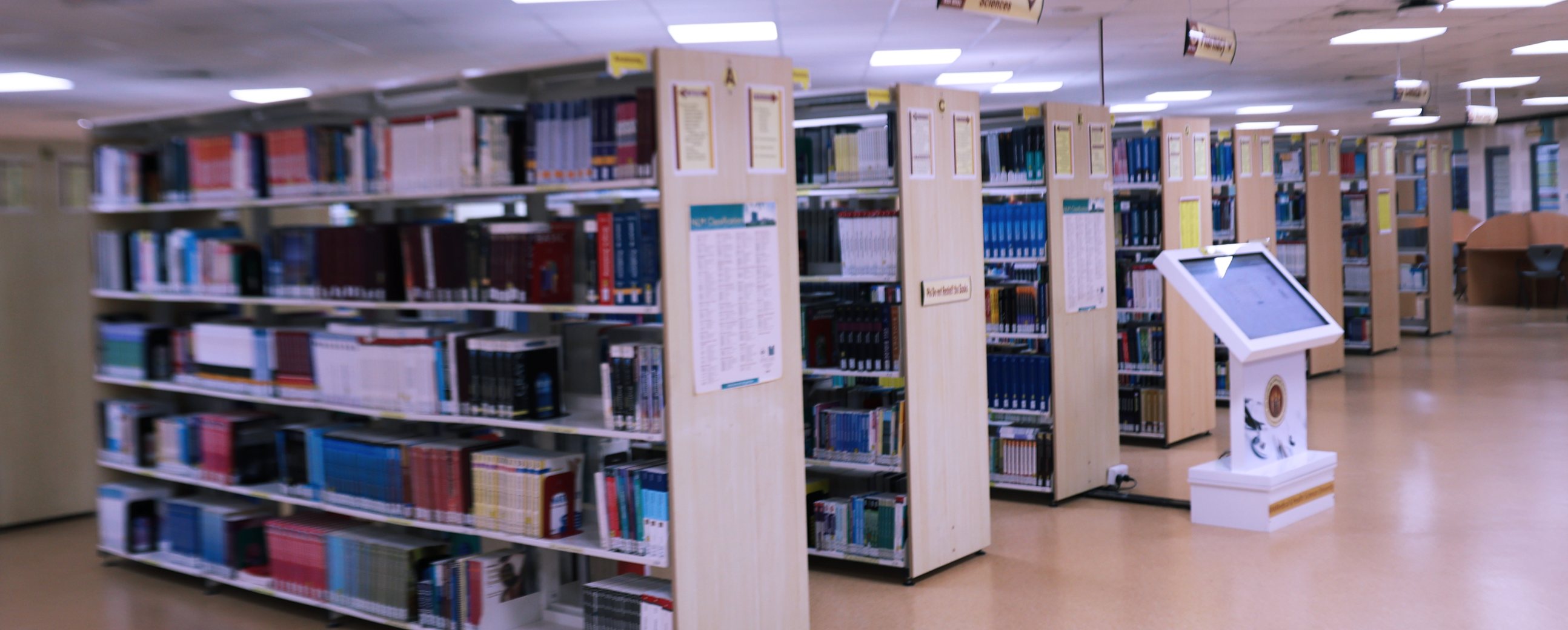 Open shelving in the RAK MHSU Library with the Sciences and Nursing collections signposted, and a catalogue search kiosk beside the aisle