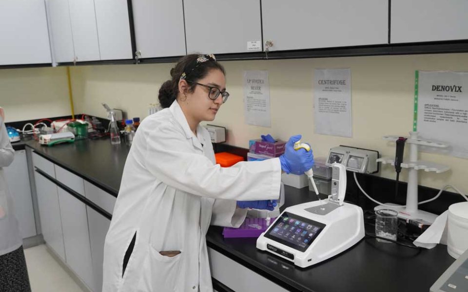 A researcher in a laboratory coat loading samples into a bench instrument at the Translational Medical Research Centre