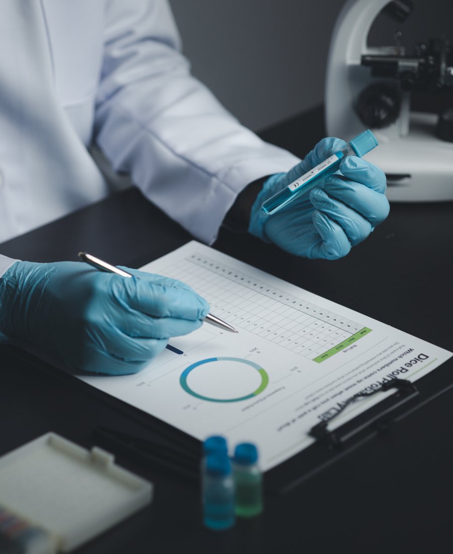 A gloved hand marking up a printed research report beside a microscope