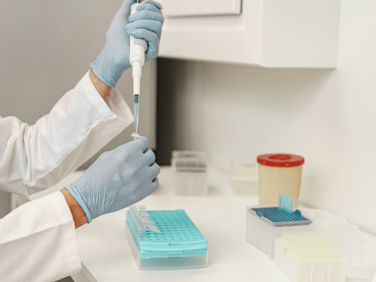A gloved hand pipetting samples into a tray of tubes on a laboratory bench